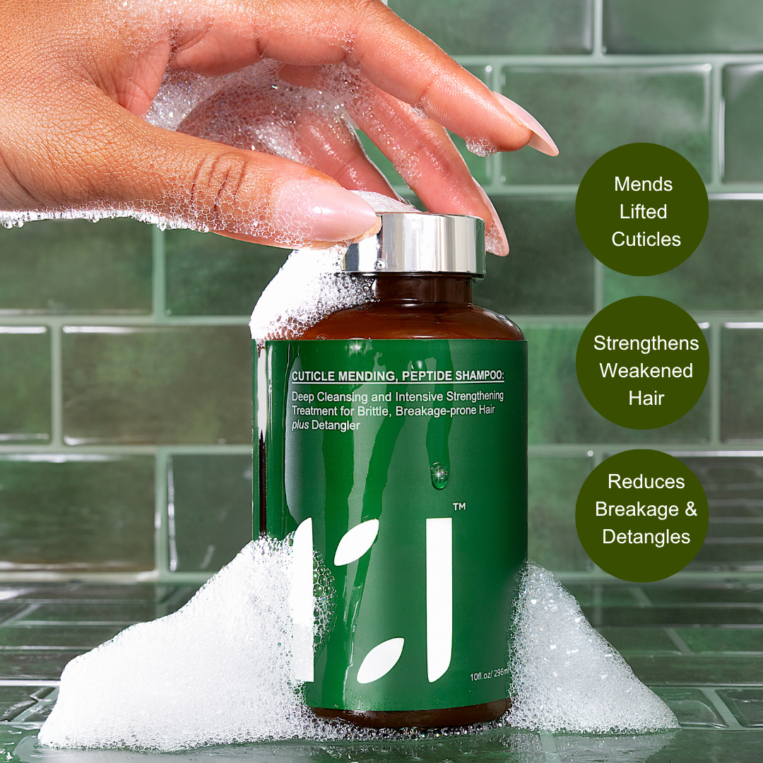 Bottle of ROOTED REVIVALL Shampoo with a hand holding it, surrounded by bubbles, against a tiled bathroom background.