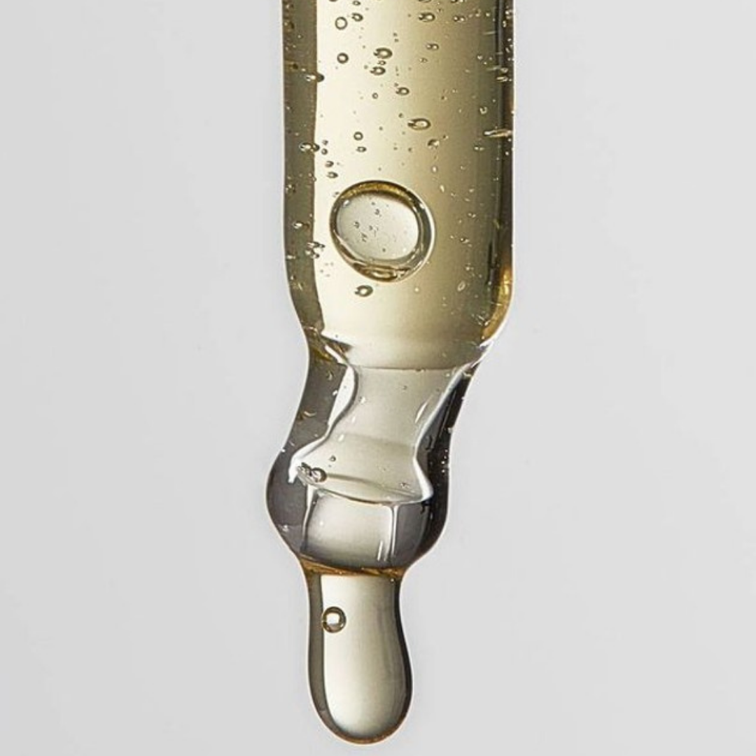 Glass dropper with a clear liquid on a light gray background