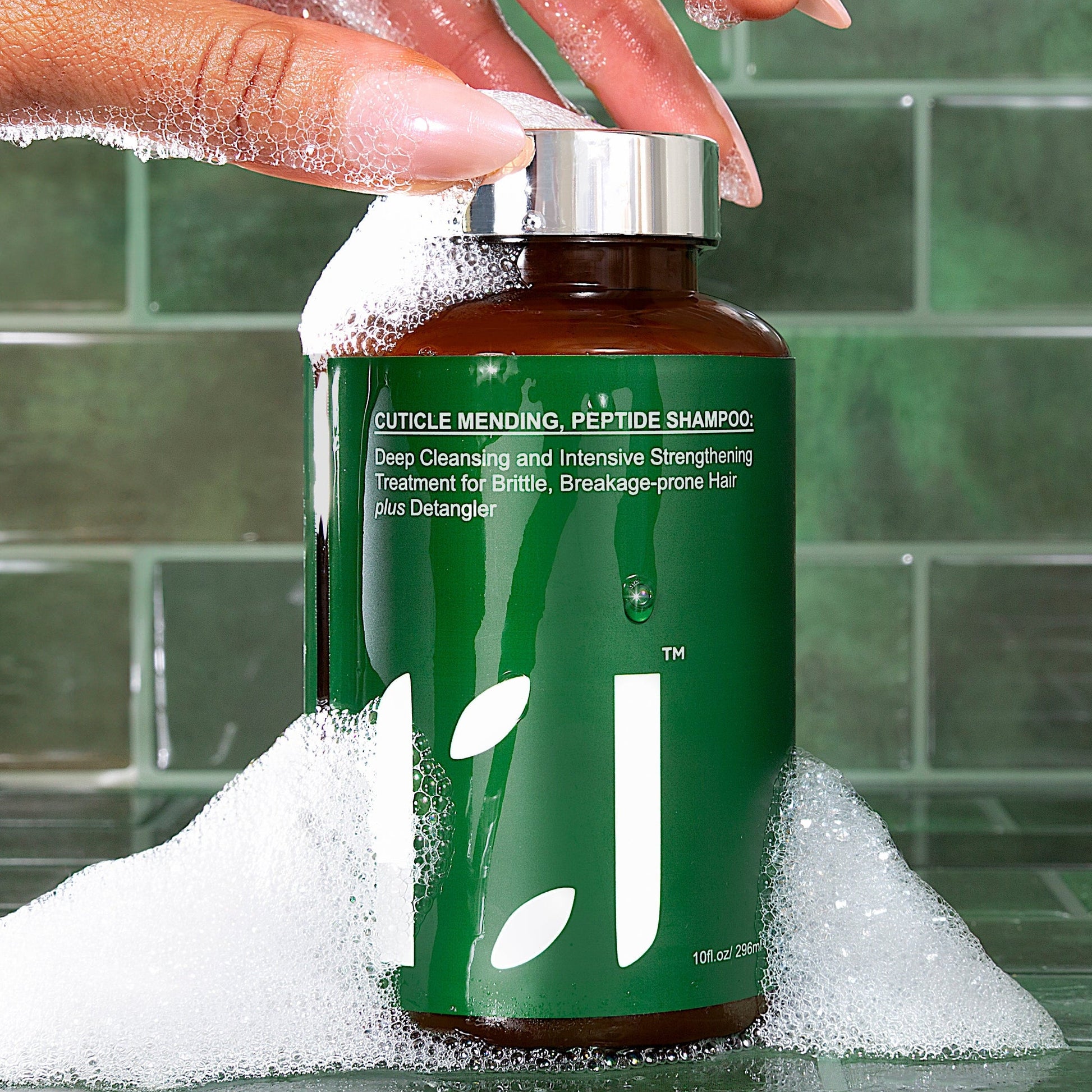 Hand holding a green shampoo bottle with bubbles on a tiled bathroom floor