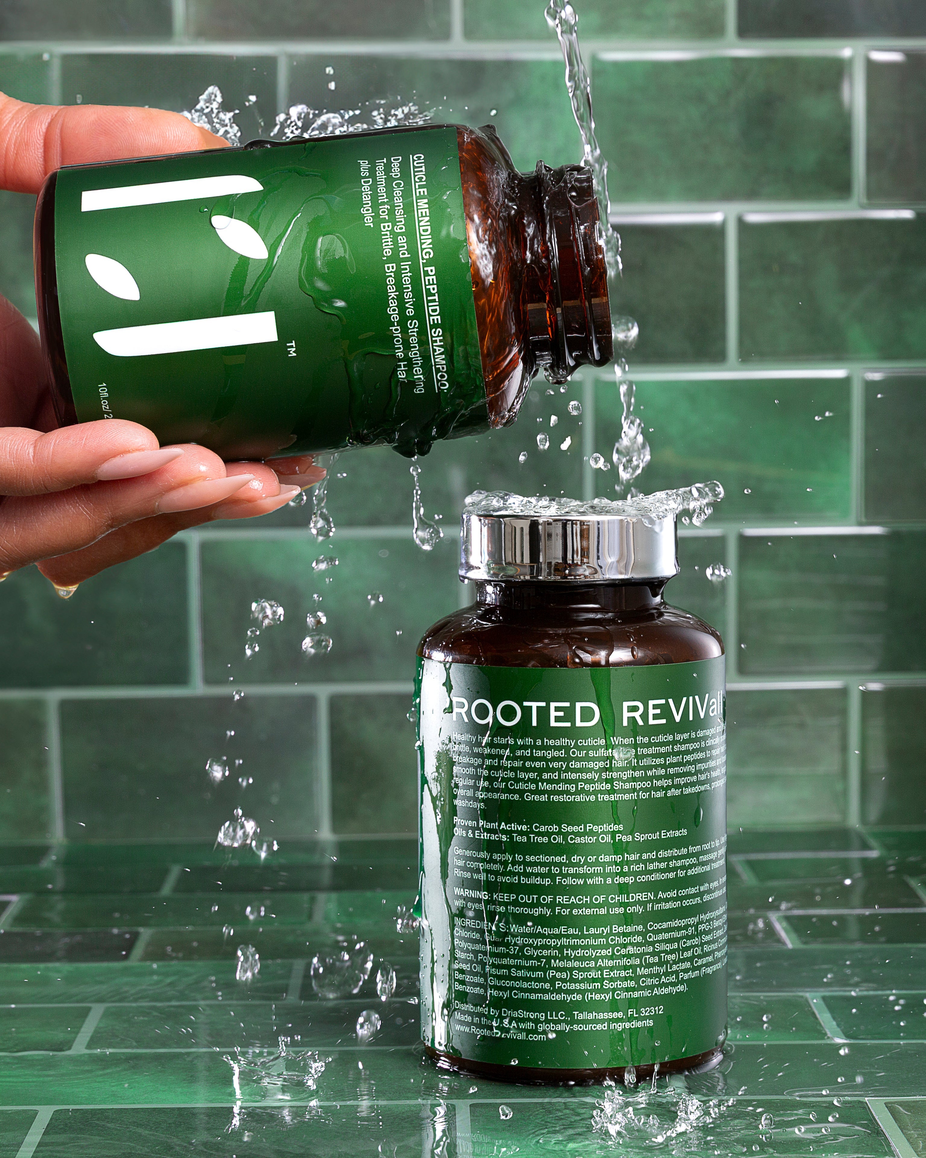 Hand pouring water from a 'Rooted Revivall' bottle onto another bottle against a green tiled wall.